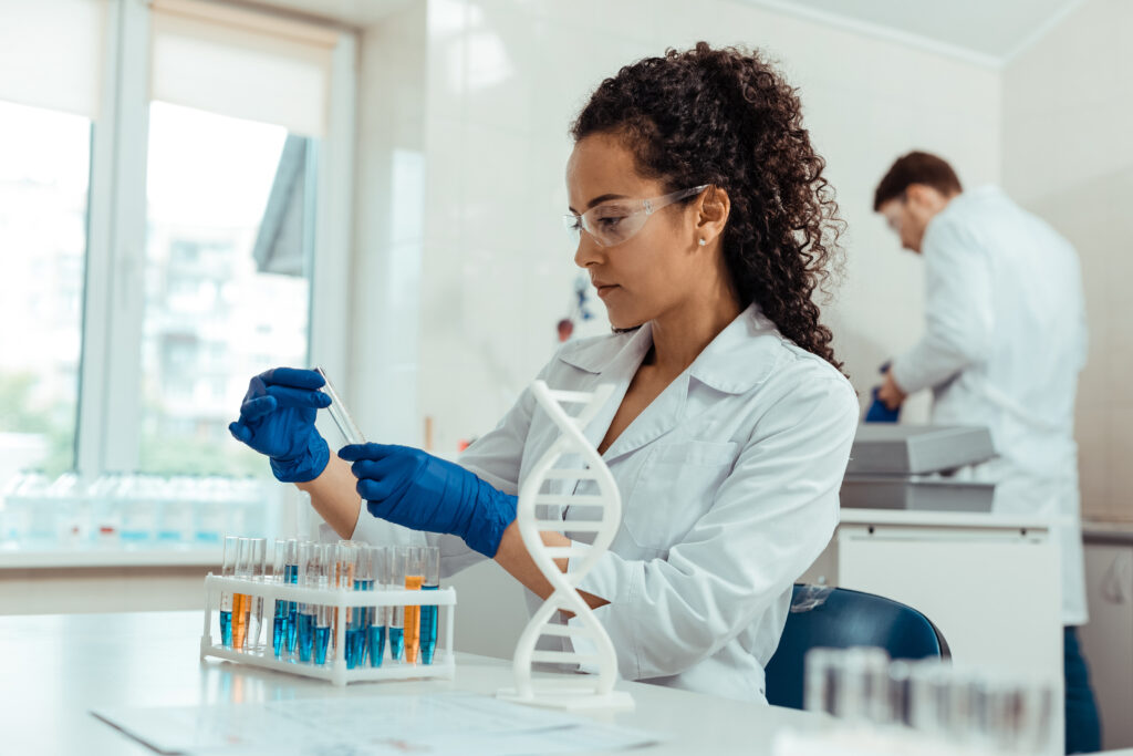 a woman in white lab coat and blue gloves holding a test tube